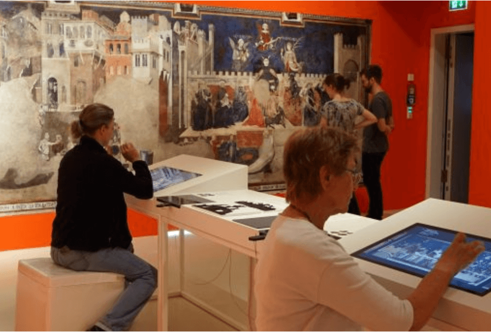 Besucherinnen und Besucher entdecken die Ausstellung des Stadtmuseums Simeonstift Trier mit interaktiven Medienstationen und historischen Wandgemälden.